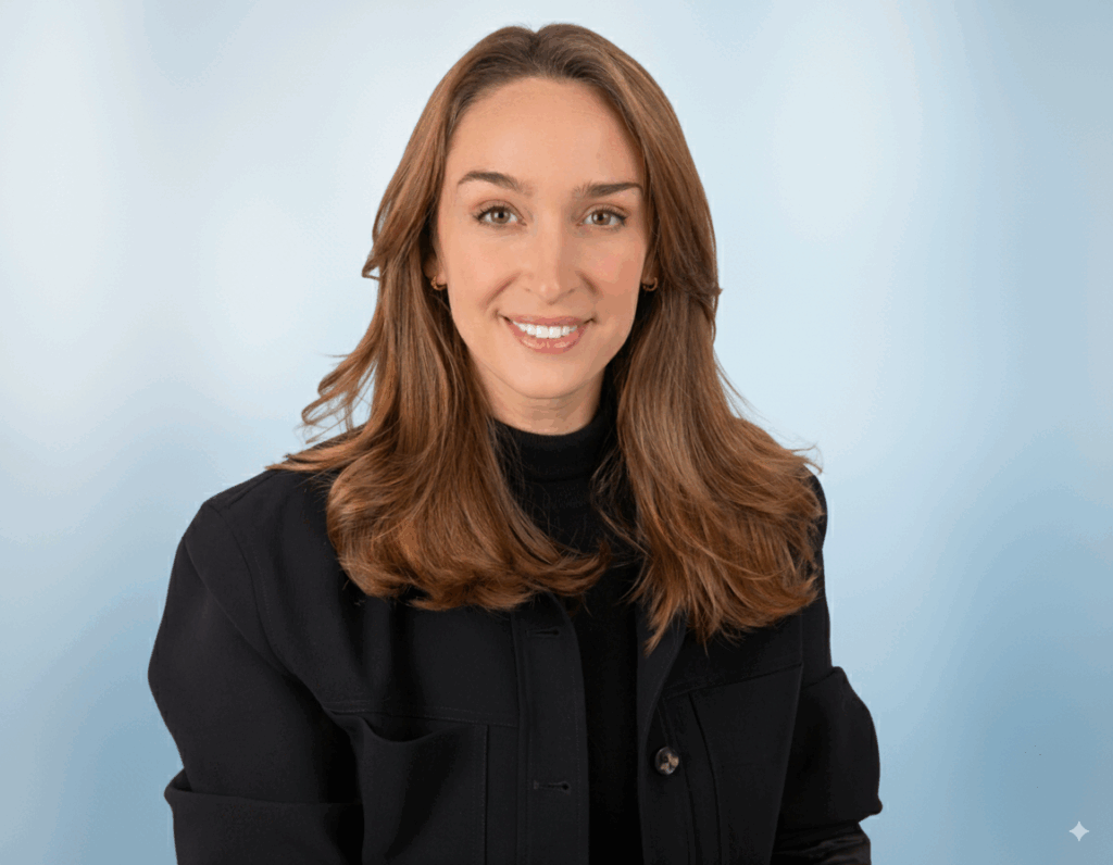 Professional indoor headshot of woman in dark blazer with light blue backdrop